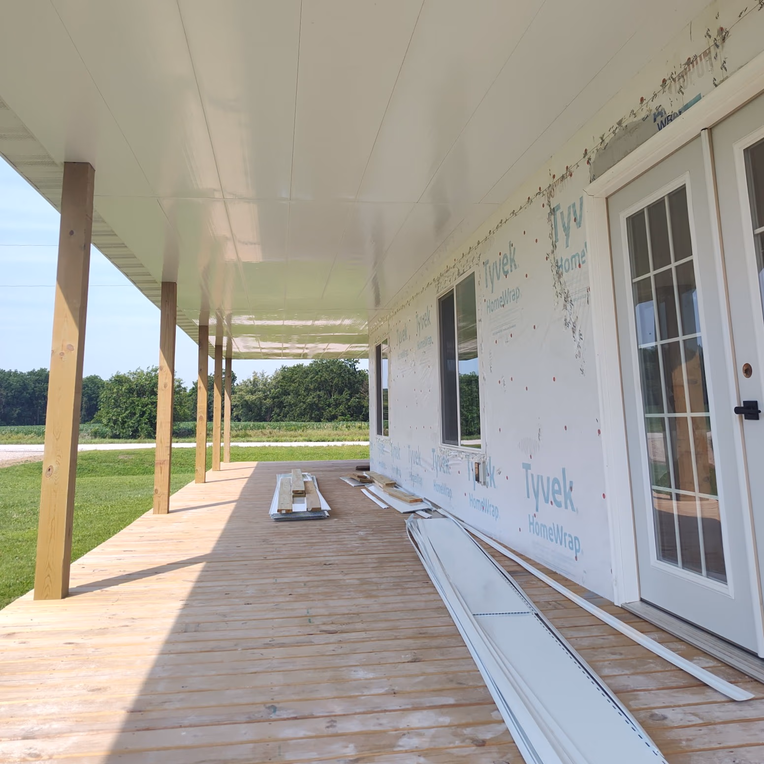 Wooden porch under construction with siding materials, Tyvek house wrap, and glass door with grid panels.