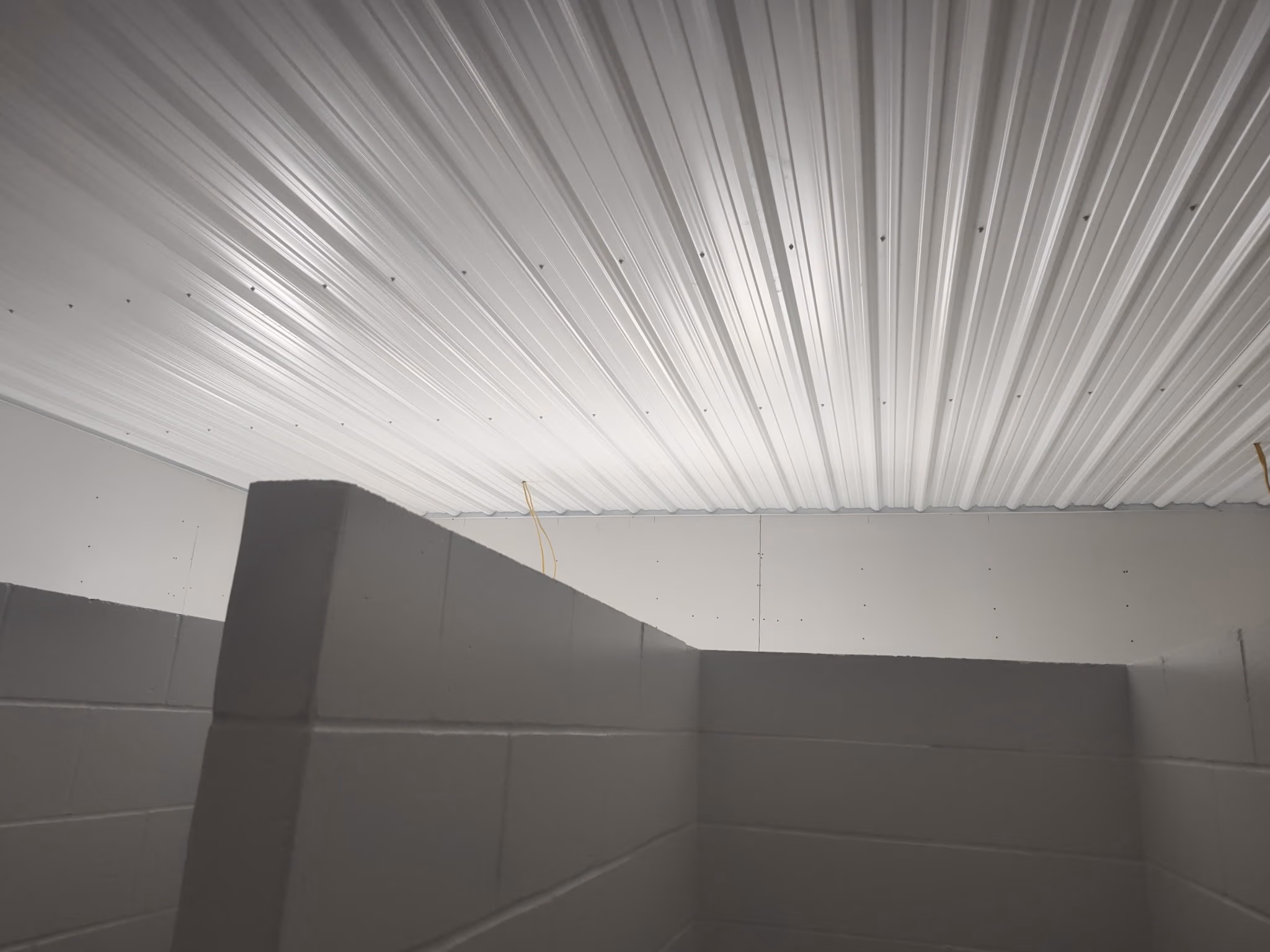 Interior view of gray concrete block walls and a white corrugated metal ceiling with exposed wiring.