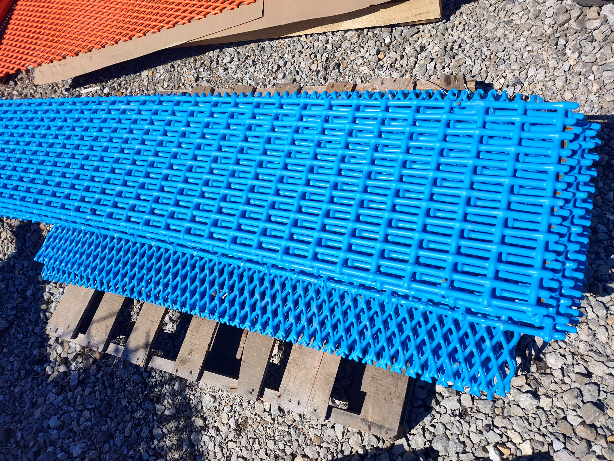Stack of bright blue plastic safety fence panels on a wooden pallet over gravel ground.